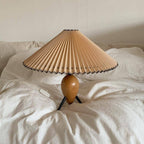 A Clérachic table lamp resting on a rumpled white duvet, its black cord running to an in-line switch.