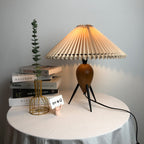 A Clérachic table lamp with stacked books and a gold wire vase on a table with a pale grey cloth.