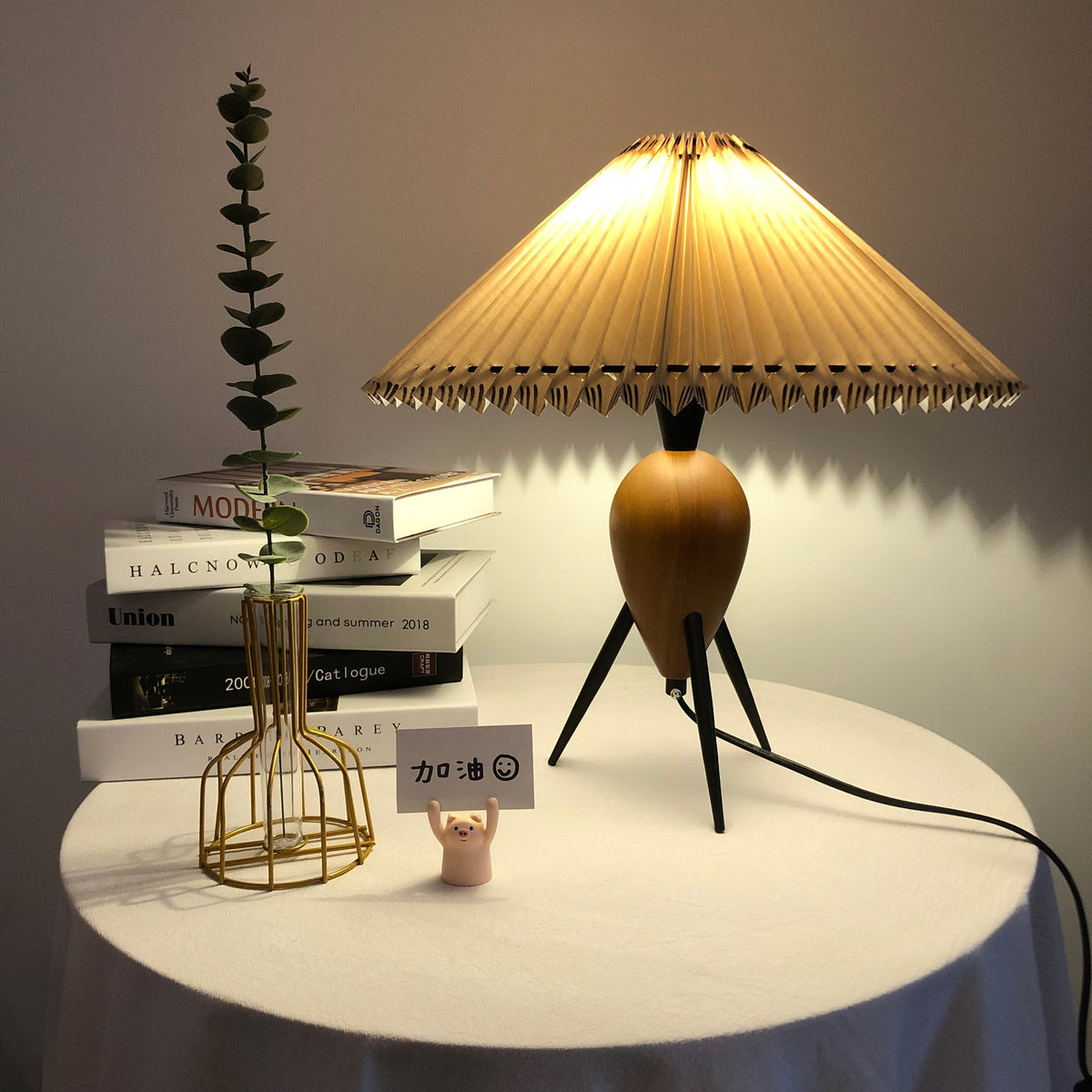 Amber light behind a gold wire vase and eucalyptus, with this Clérachic table lamp glowing on a draped round table.