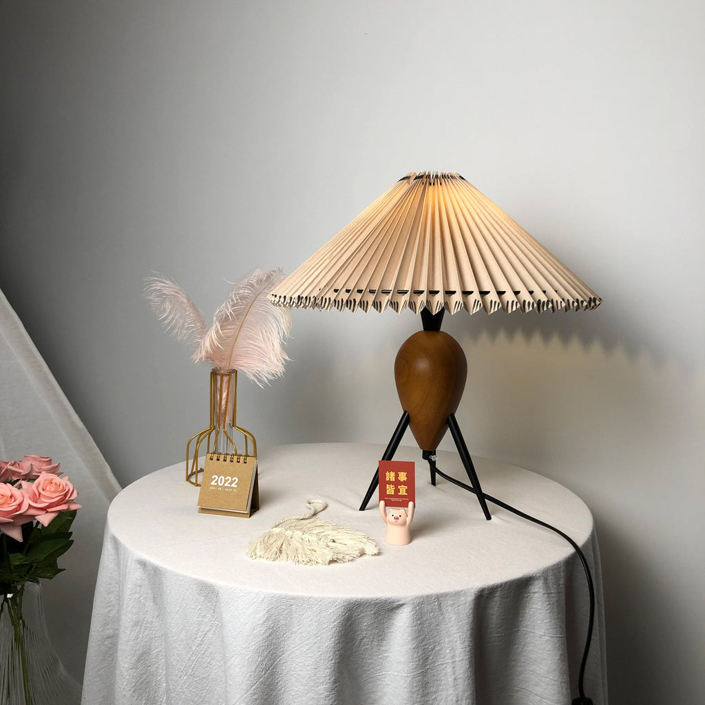 Lit Clérachic table lamp beside pink roses in the corner, a feather vase and a desk calendar on a white round table.