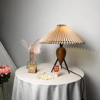 Lit Clérachic table lamp beside pink roses in the corner, a feather vase and a desk calendar on a white round table.