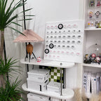 A Clérachic table lamp on a white shelf unit with display boxes, a calendar board and shelves of small figures behind.
