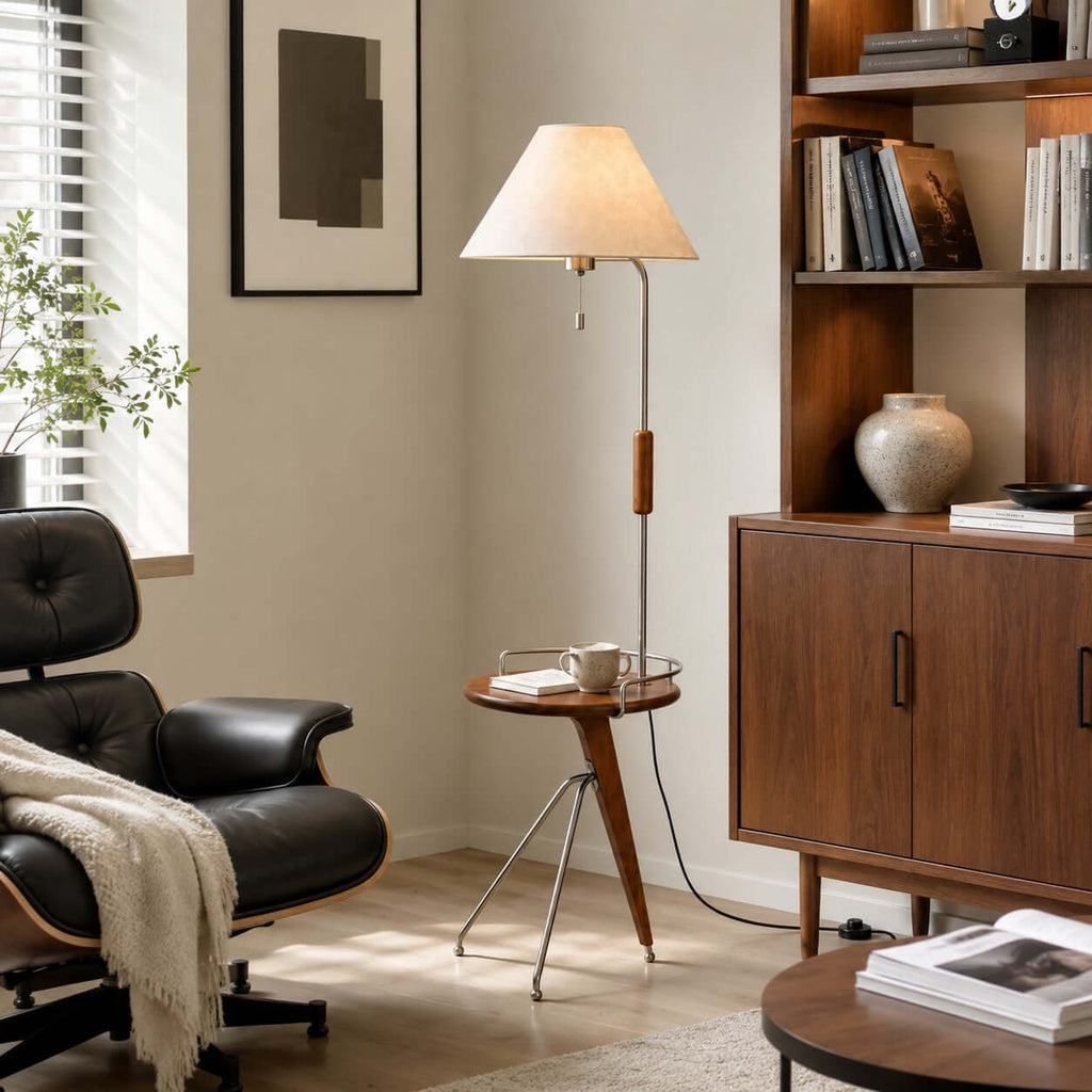 A Clérachic floor lamp with a built-in walnut tray holding a cup, beside a black leather lounge chair and a wooden bookcase.