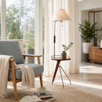 Shown here, a Clérachic floor lamp with a tray table holding a small vase, beside a blue-grey armchair and sheer curtains.