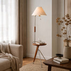 Tray of this Clérachic floor lamp holding a glass and a book, next to a cream sofa and a vase of dried stems.