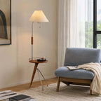 Beige-shaded Clérachic floor lamp with a tray table by a window, next to a blue-grey lounge chair and a knitted throw.