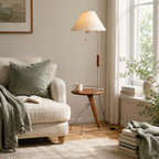 In this photo, a Clérachic floor lamp with a wood tray table beside a boucle armchair with an olive cushion and a window.