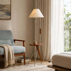This Clérachic floor lamp with a tray table and a mug, beside a pale blue armchair and a cream pouffe.