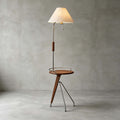 A Clérachic floor lamp with a beige shade and walnut tray table on a polished concrete floor against a grey wall.