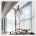 The Clérachic Trove in brass hung in a double-height sitting room beside sheer-curtained windows.