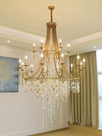 The Clérachic Trove in brass lit above a dining room, its glow picking up the green drapes behind.