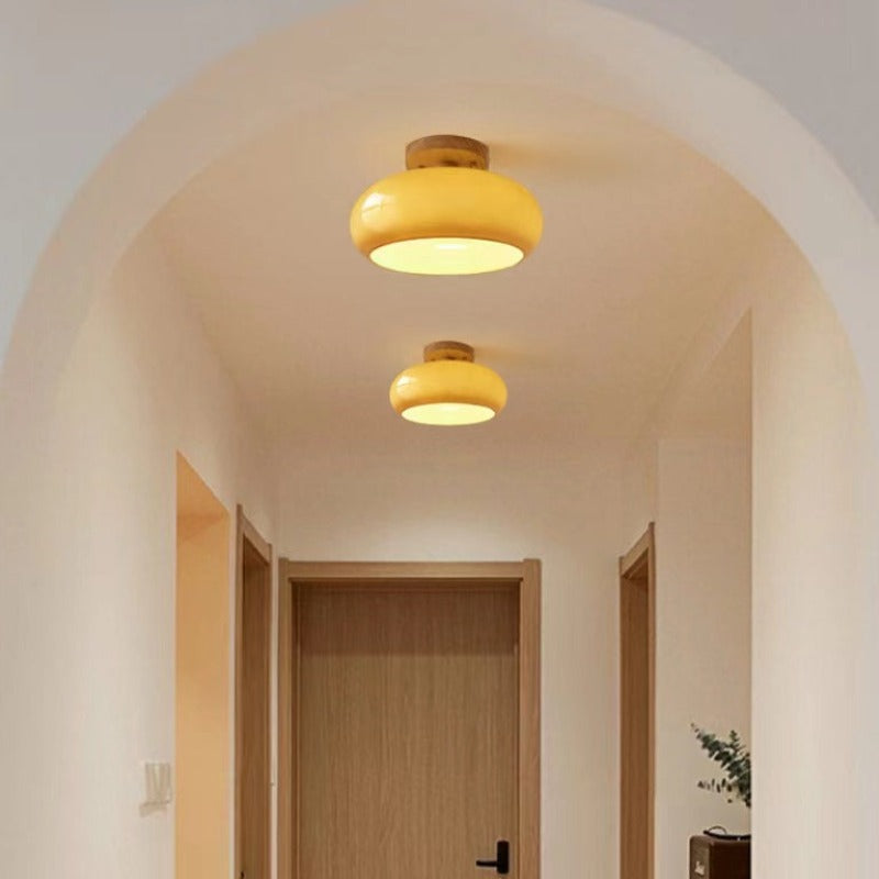 Two Clérachic turned wood ceiling lights in mustard glass lighting an arched hallway above a pale oak door.
