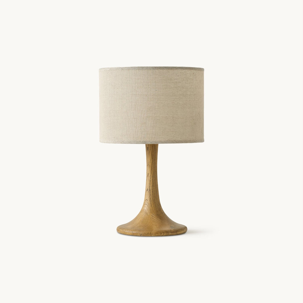 A Clérachic table lamp on a plain white backdrop, with a beige linen drum shade on a slim turned-wood column and a flared wooden foot.