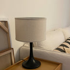 Close side view of this Clérachic table lamp in black, standing on a wooden tray beside a cream sofa with a striped cushion.