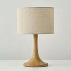 Unlit Clérachic table lamp with a wood-coloured turned column and flared base, under a wide beige linen drum shade.