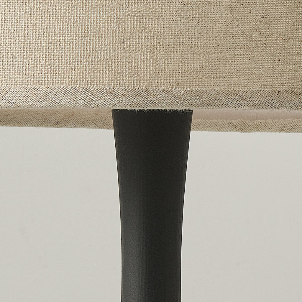 Close view of the black turned column of this Clérachic table lamp meeting the underside of its woven beige drum shade.
