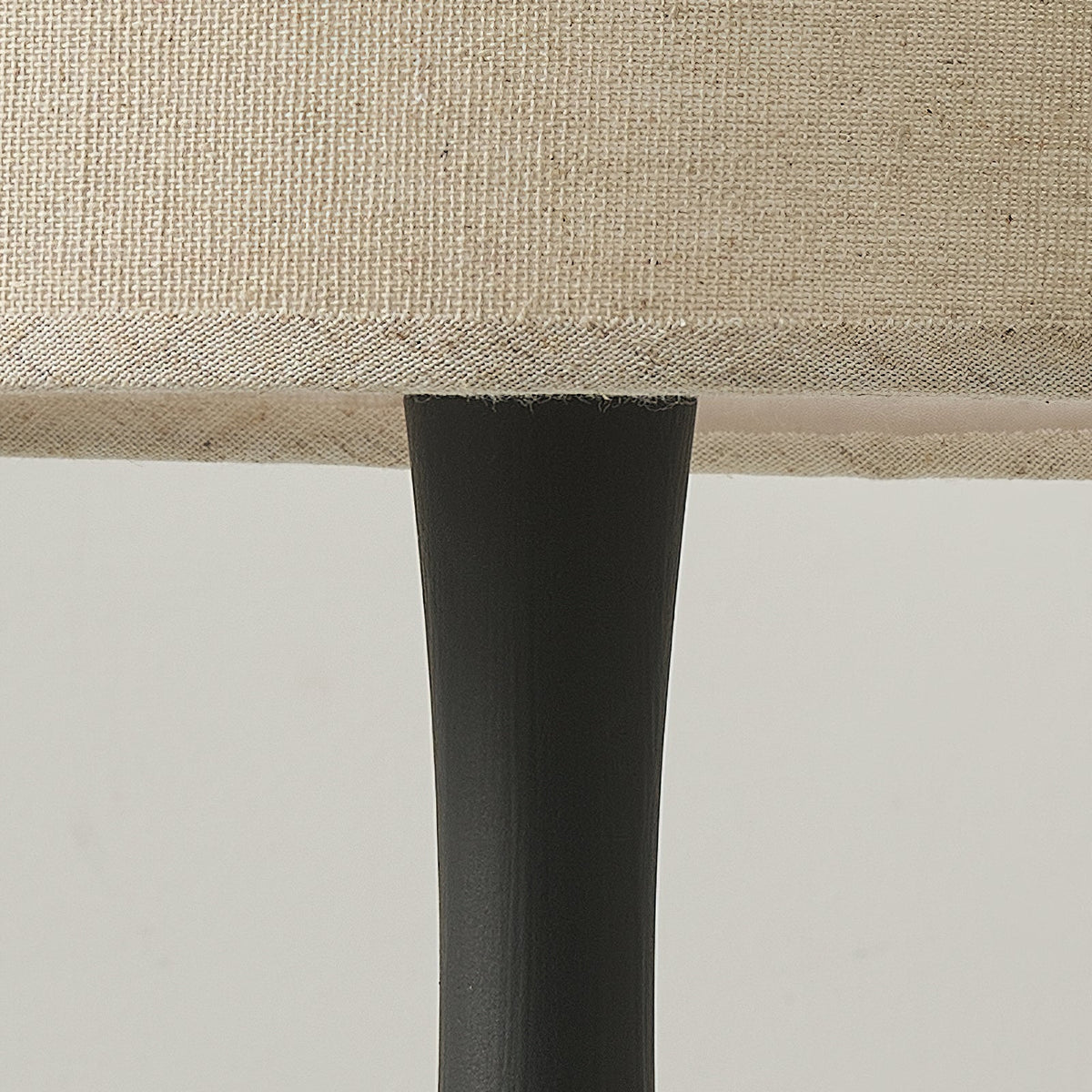 Close view of the black turned column of this Clérachic table lamp meeting the underside of its woven beige drum shade.