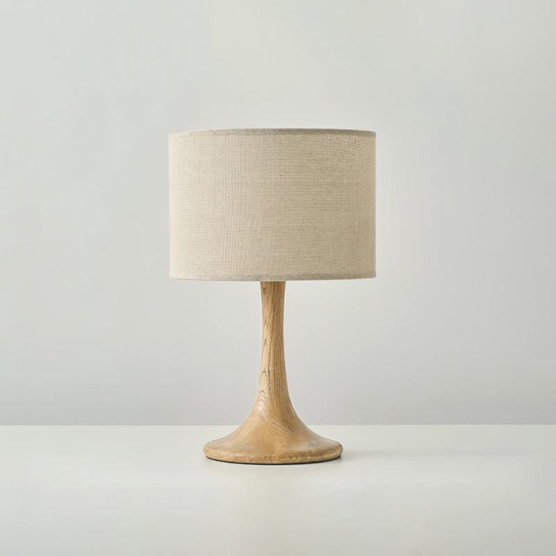 Front view of this Clérachic table lamp in a wood colour, with a beige woven drum shade above a flared turned-wood foot.