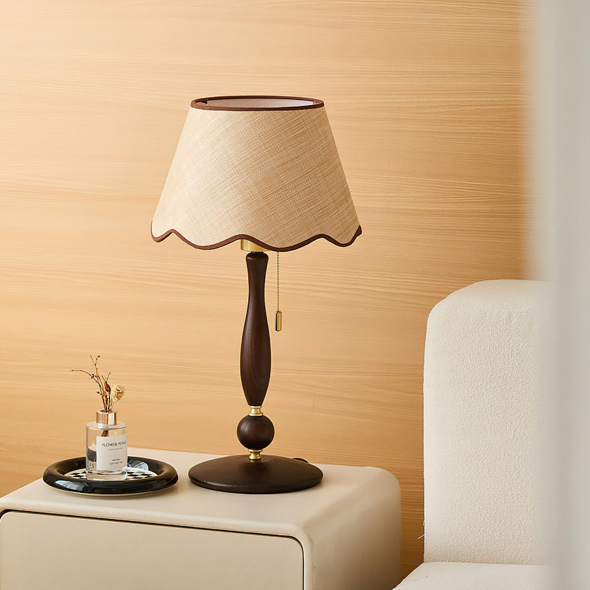 A Clérachic table lamp stands on a cream bedside cabinet in front of an oak-panelled wall, with a small scent bottle on a dark tray.