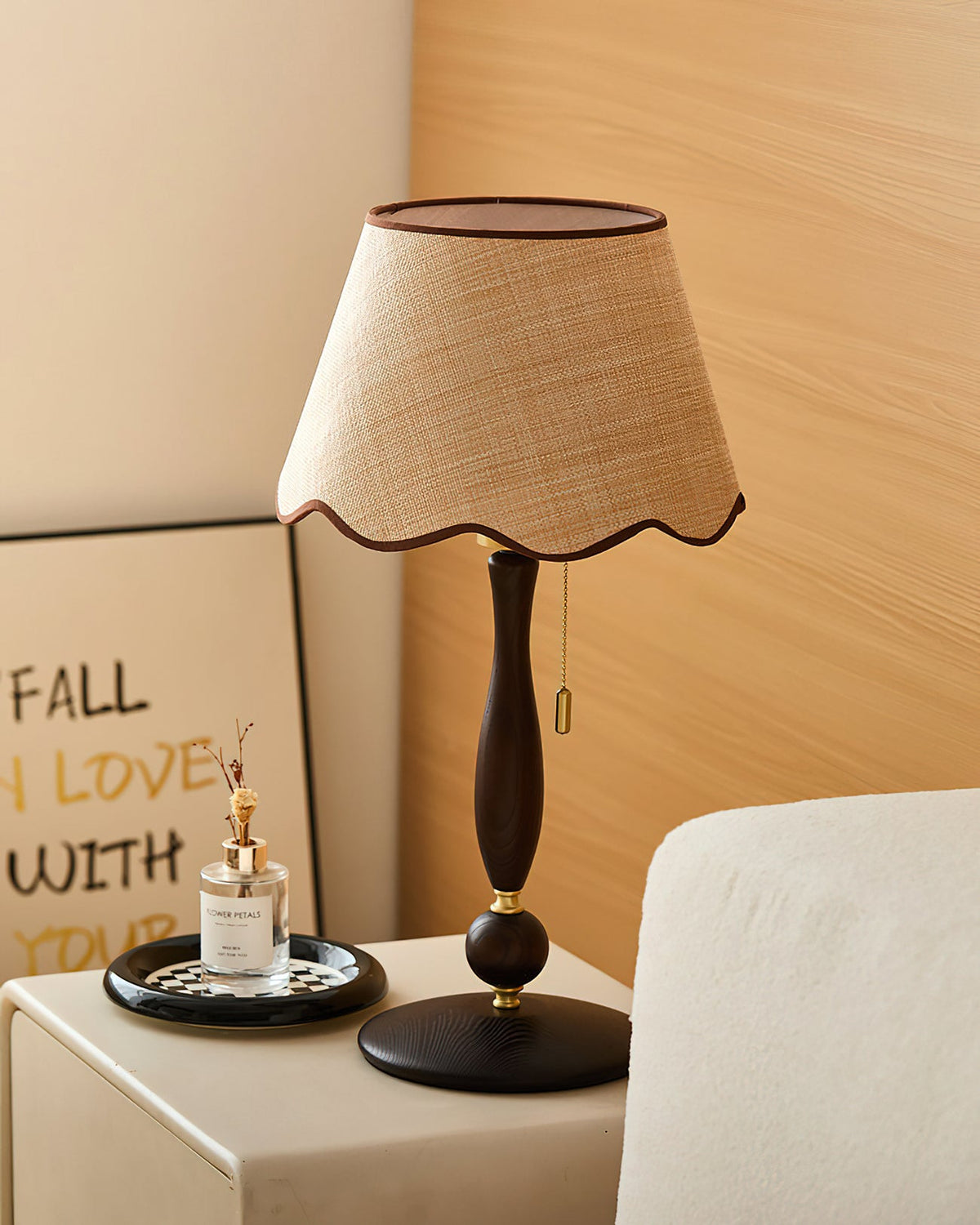 A lamp with a brass pull chain stands on a cream cabinet in front of an oak wall, with a framed lettered print behind; a Clérachic design.
