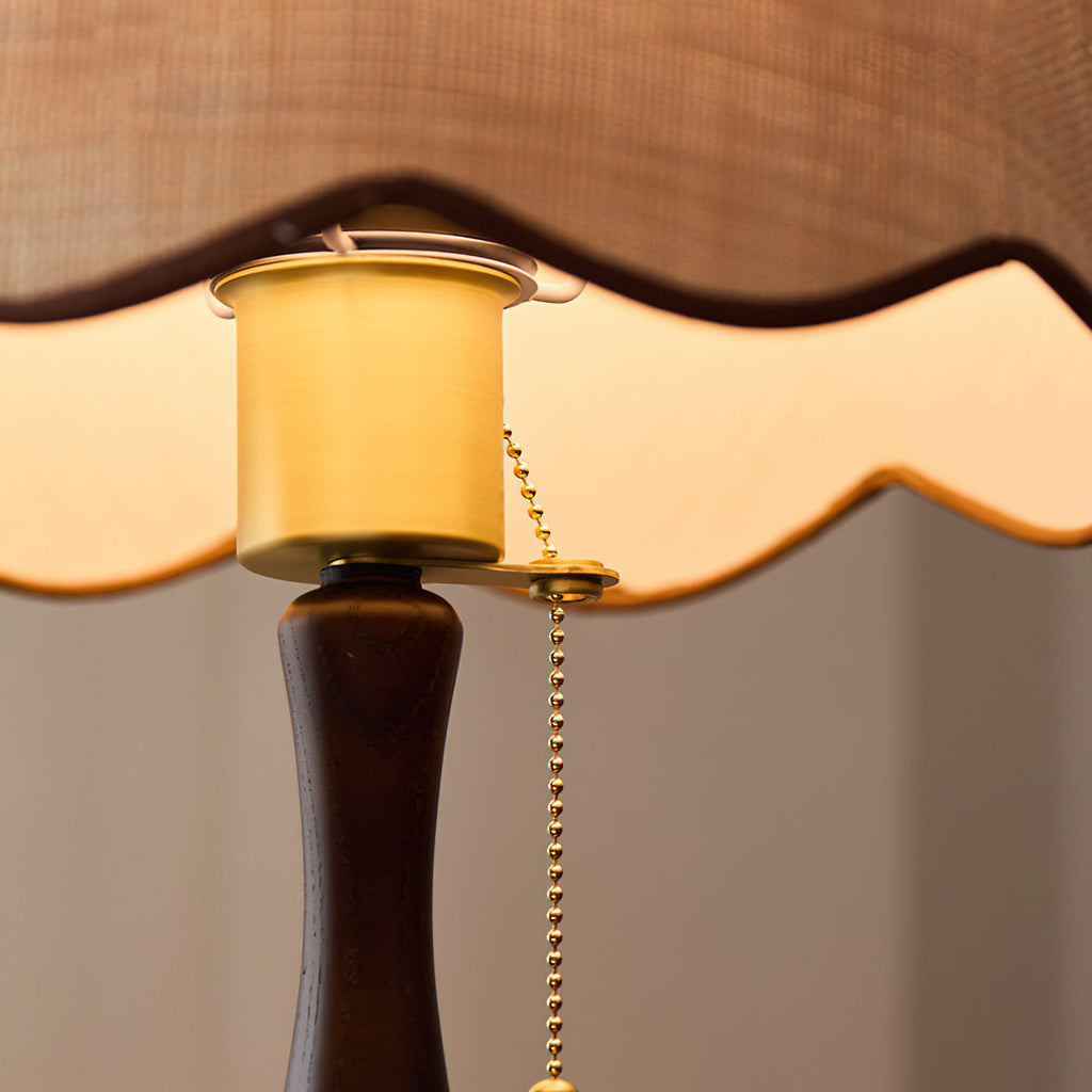 Close view of the brass-toned socket, the brass pull chain and the scalloped shade edge, above the walnut stem; a Clérachic lamp.