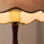 Close view of the brass-toned socket, the brass pull chain and the scalloped shade edge, above the walnut stem; a Clérachic lamp.