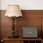 Scalloped shade and turned walnut stem on a wooden chest next to a black speaker, against a walnut wall; from Clérachic.