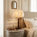 Bedside scene with a Clérachic table lamp lit on a pale grey drawer unit, a hand mirror and books at its foot.