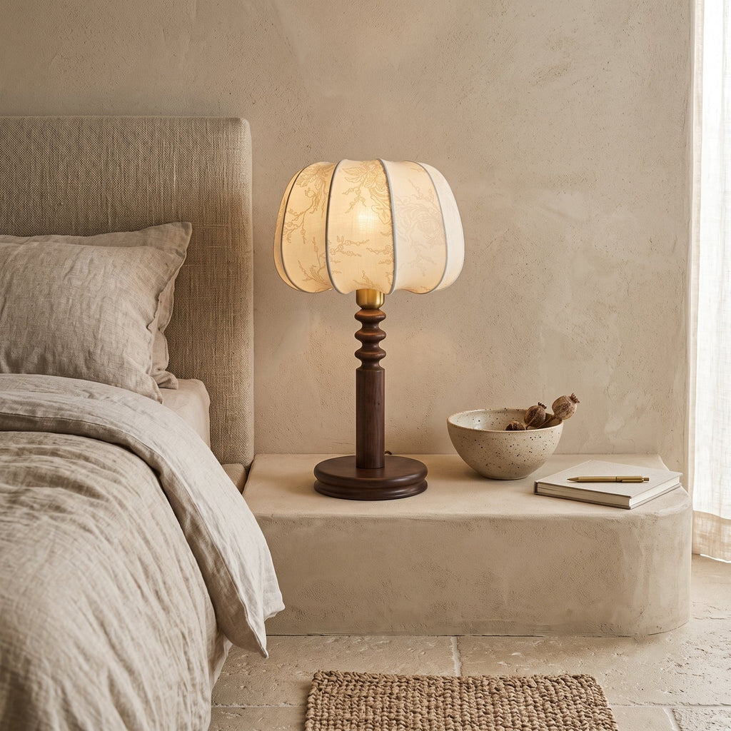 A Clérachic table lamp on a plaster ledge beside a linen-dressed bed, with a small bowl and notebook next to the base.