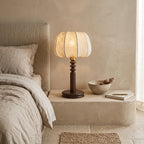 A Clérachic table lamp on a plaster ledge beside a linen-dressed bed, with a small bowl and notebook next to the base.