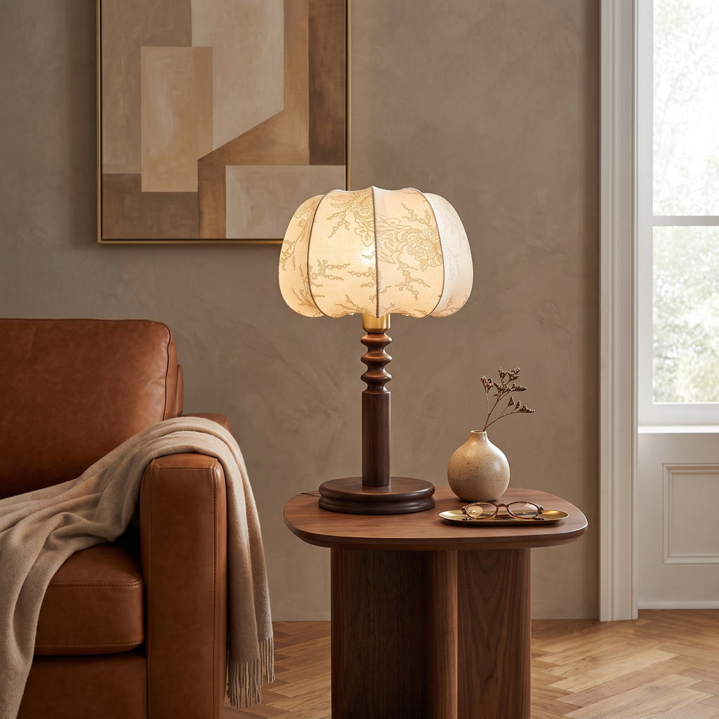 Warm light from a Clérachic table lamp on a round walnut side table, beside a tan leather armchair and a small bud vase.