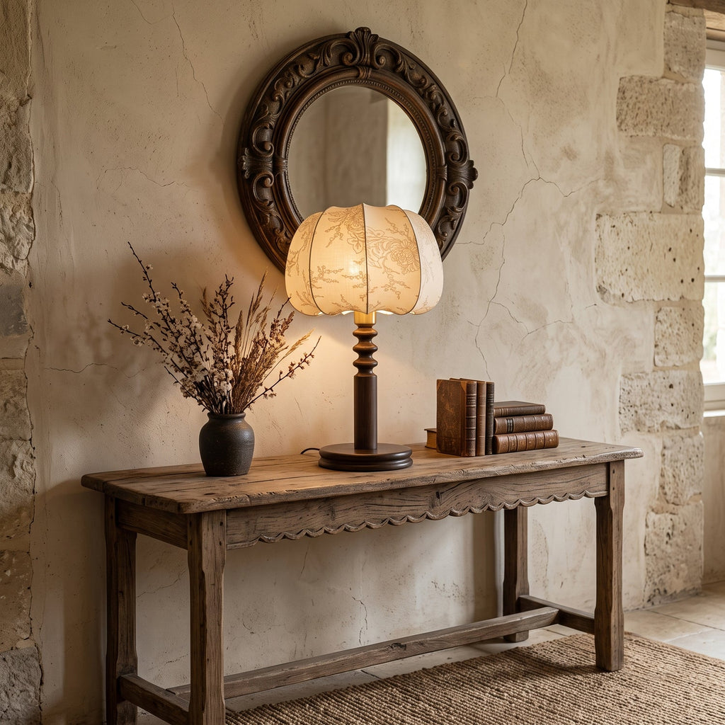 On a rustic wooden console under a round carved mirror, this Clérachic table lamp sits beside dried branches and stacked books.