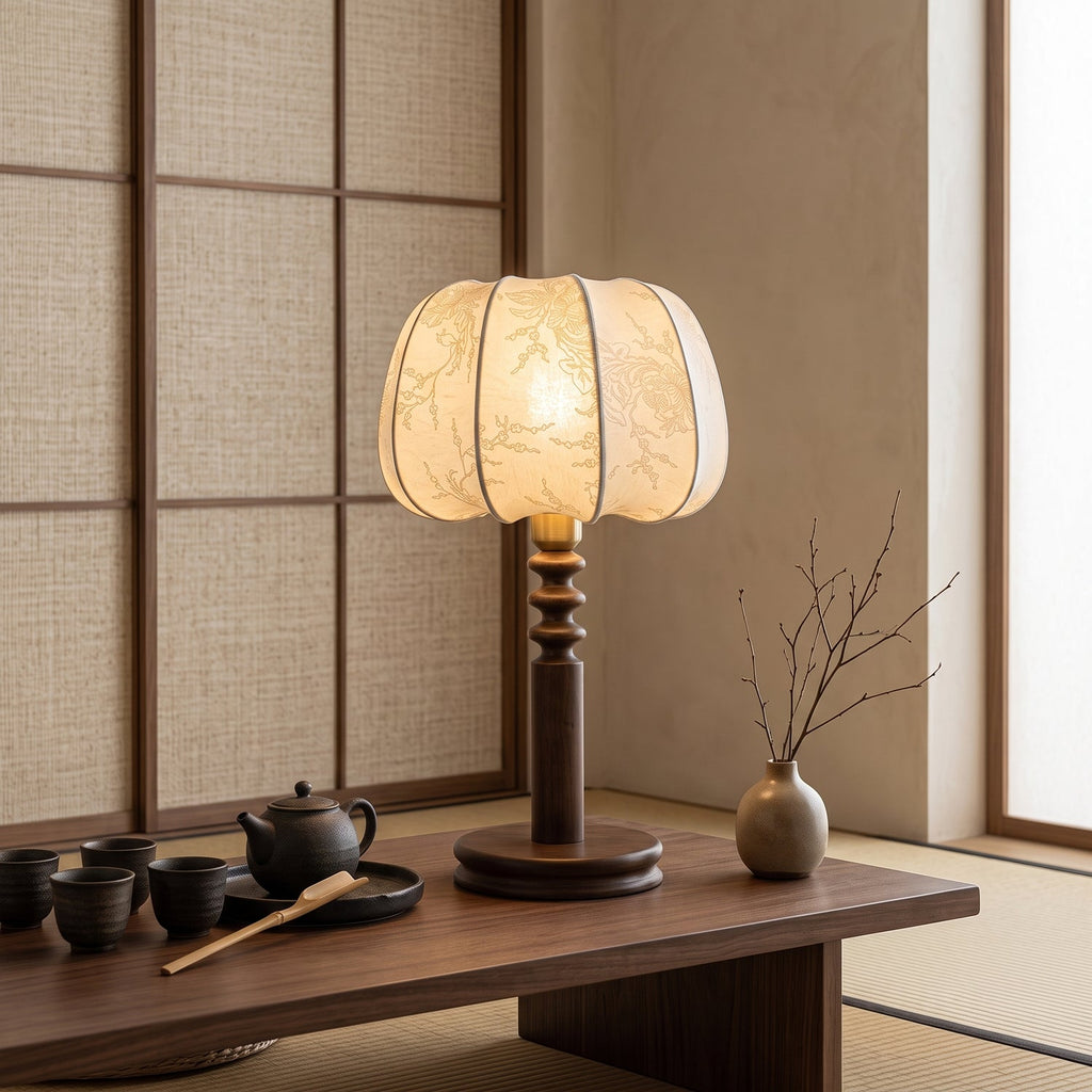 Clérachic table lamp lit on a low wooden table with a tea set and a branch in a vase, in front of a woven screen.