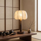 Clérachic table lamp lit on a low wooden table with a tea set and a branch in a vase, in front of a woven screen.