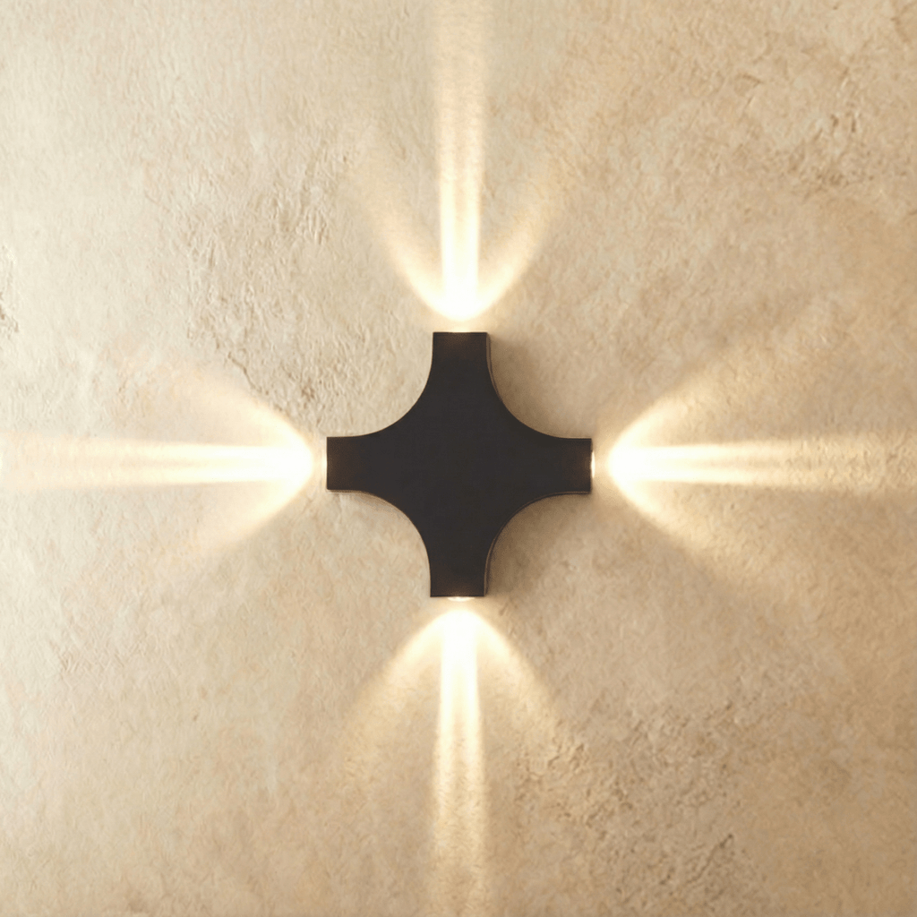 The four-head Clérachic outdoor wall light casts warm beams in every direction from its black cross-shaped body.