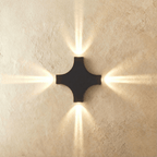 The four-head Clérachic outdoor wall light casts warm beams in every direction from its black cross-shaped body.