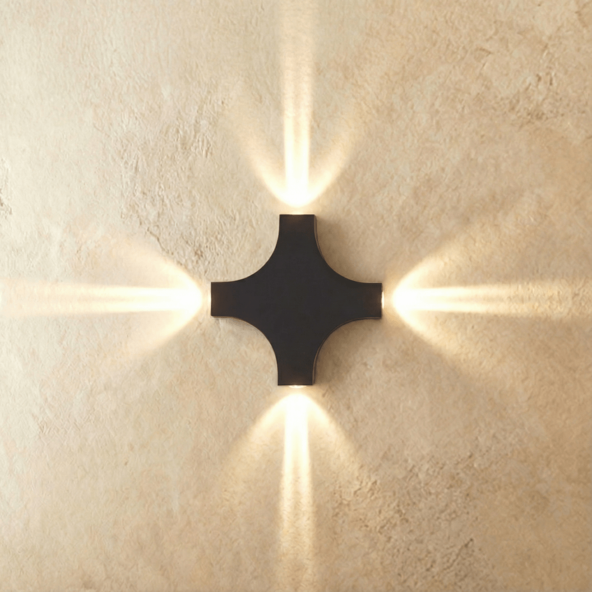 The four-head Clérachic outdoor wall light casts warm beams in every direction from its black cross-shaped body.