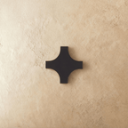 This cross-shaped Clérachic outdoor wall light in matte black aluminium sits flush against a plastered wall, unlit.