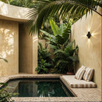 Beside a tiled plunge pool, the cross-shaped Clérachic outdoor wall light glows warmly among tropical palms.
