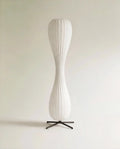 Clérachic twisted hourglass floor lamp with a ribbed paper-style shade on a black four-legged metal base, unlit on pale grey.
