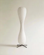 Clérachic twisted hourglass floor lamp with a ribbed paper-style shade on a black four-legged metal base, unlit on pale grey.