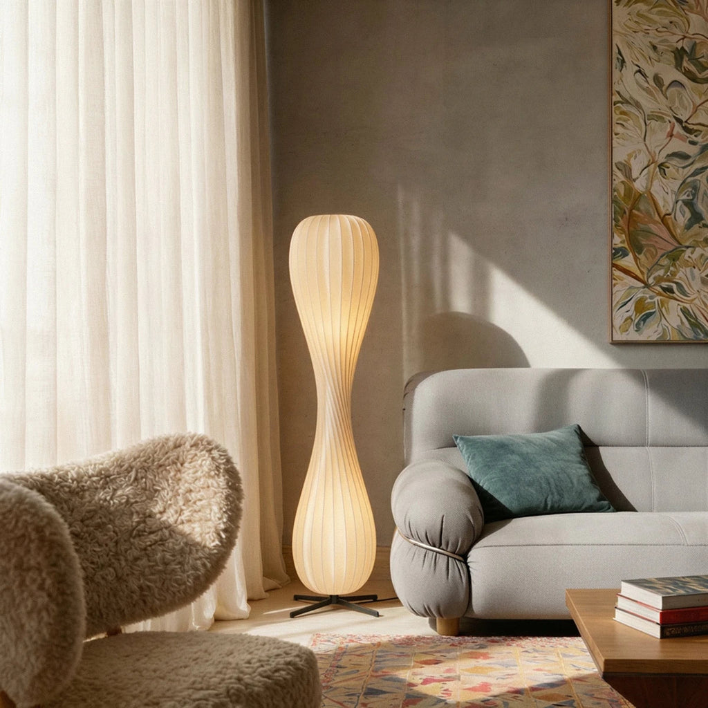 Clérachic twisted floor lamp glowing beside a grey sofa and a shearling armchair, with sheer curtains and a framed print.