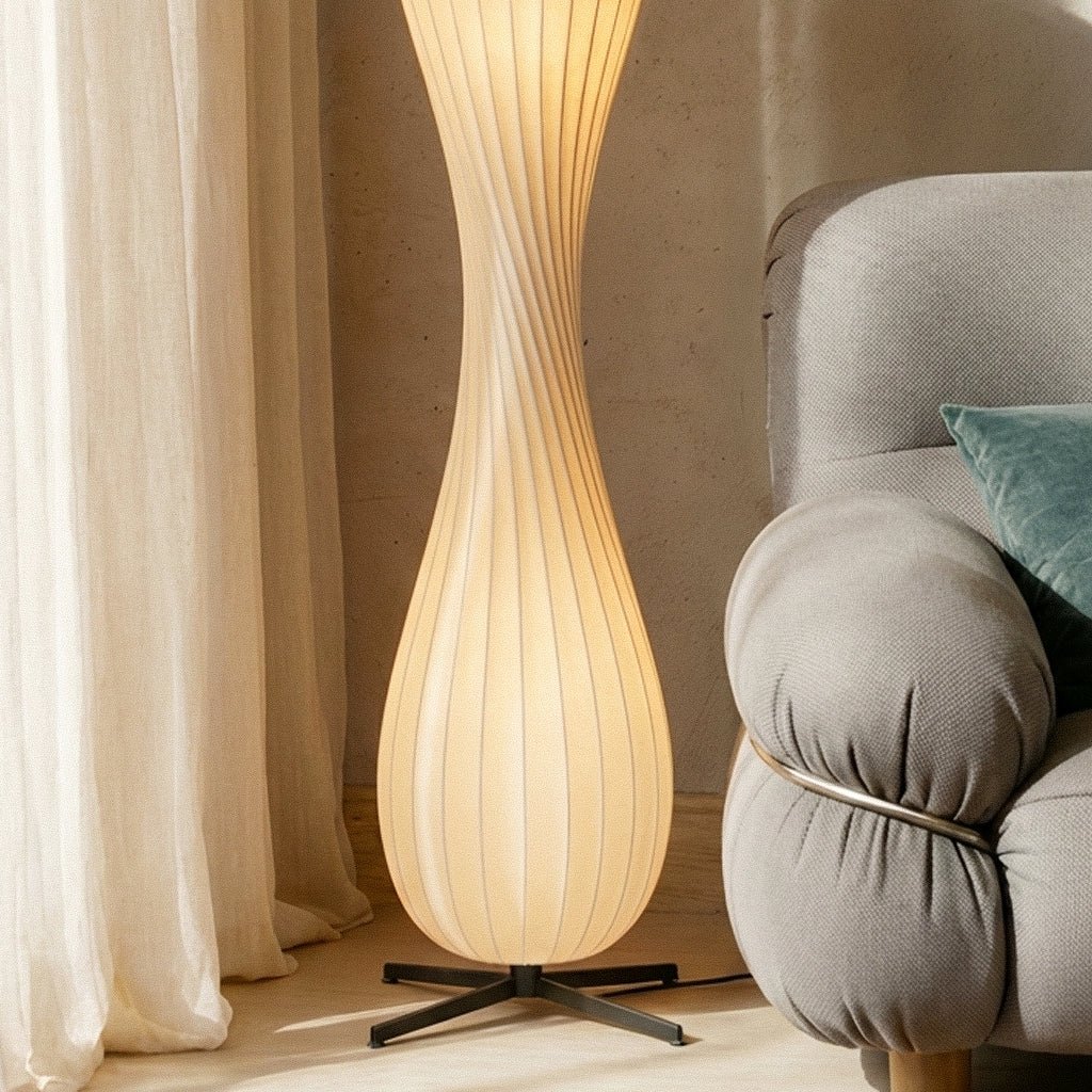 Clérachic floor lamp lit in a sunny corner, its ribbed shade between linen curtains and a grey bouclé sofa arm.