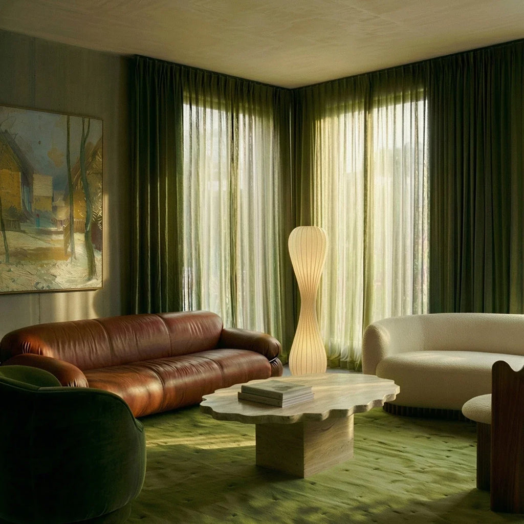 Clérachic twisted floor lamp lit in a living room with green velvet curtains, a tan leather sofa and a wavy stone table.