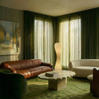 Clérachic twisted floor lamp lit in a living room with green velvet curtains, a tan leather sofa and a wavy stone table.