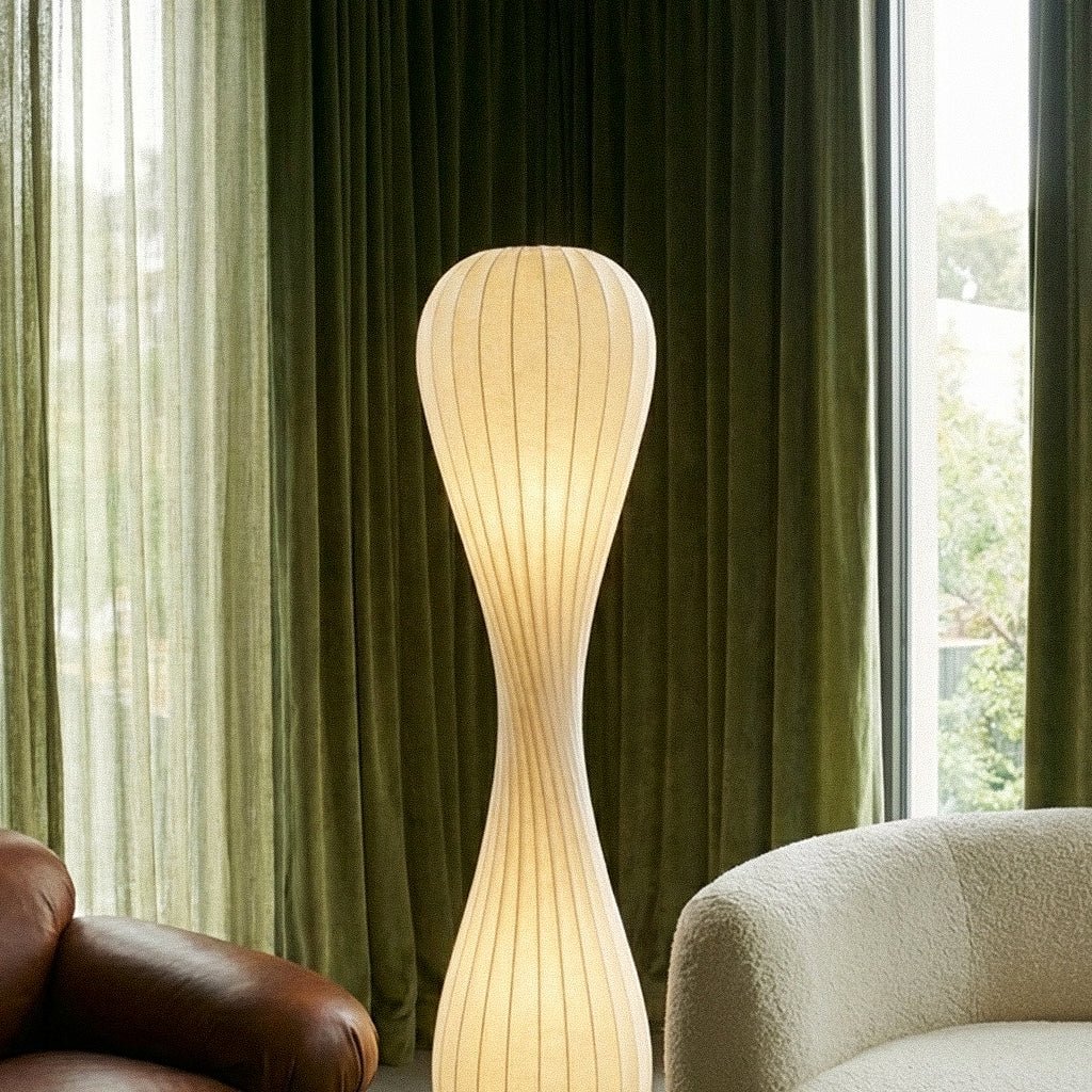 Clérachic tall ribbed floor lamp glowing in front of green velvet curtains, beside a cream bouclé sofa.