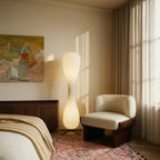 Clérachic twisted floor lamp lit in a bedroom corner beside a walnut sideboard, cream armchair and a pink patterned rug.