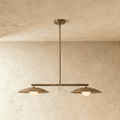 Clérachic pendant light in darkened aged brass, hung dead-centre against a mottled lime-washed wall with a white sphere under each shallow disc shade.