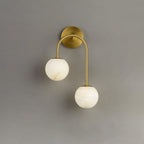 Clérachic Two-Globe Alabaster Wall Sconce in brass on a plain grey wall, its high and low stone globes staggered along one curved arm.