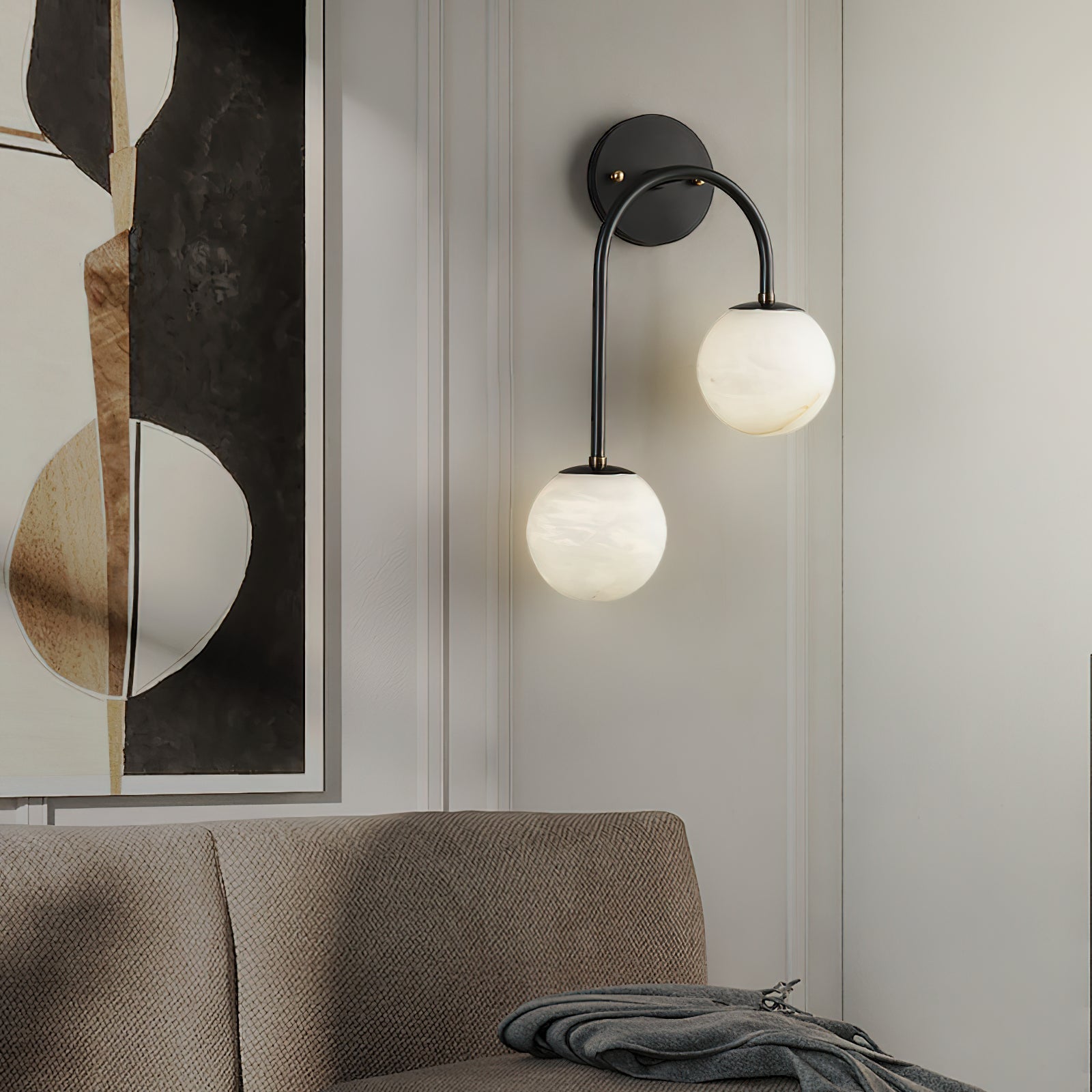 A black Clérachic Two-Globe Alabaster Wall Sconce lighting a panelled living-room wall above a linen sofa, beside a large abstract artwork.